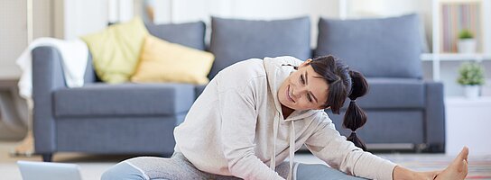 Eine junge Frau macht vor dem Laptop Gymnastik