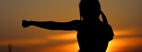 Die Silhoutte einer Frau in einer Tai Chi Pose vor einem Sonnenuntergang.