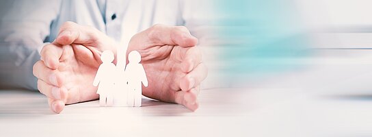 Zwei Hände liegen schützend um zwei menschliche Figuren aus Papier